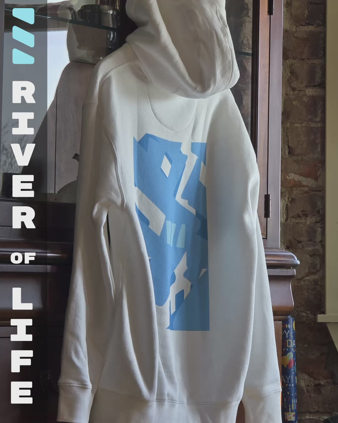 Load video: Video featuring an animated preview of a white hoodie hanging on a coat hangar, with the back facing the camera. The River of Life is printed in bright blue on its back. The Video features animations using photos and the brekky logo in different shades of blue, moving in time with the music playing.