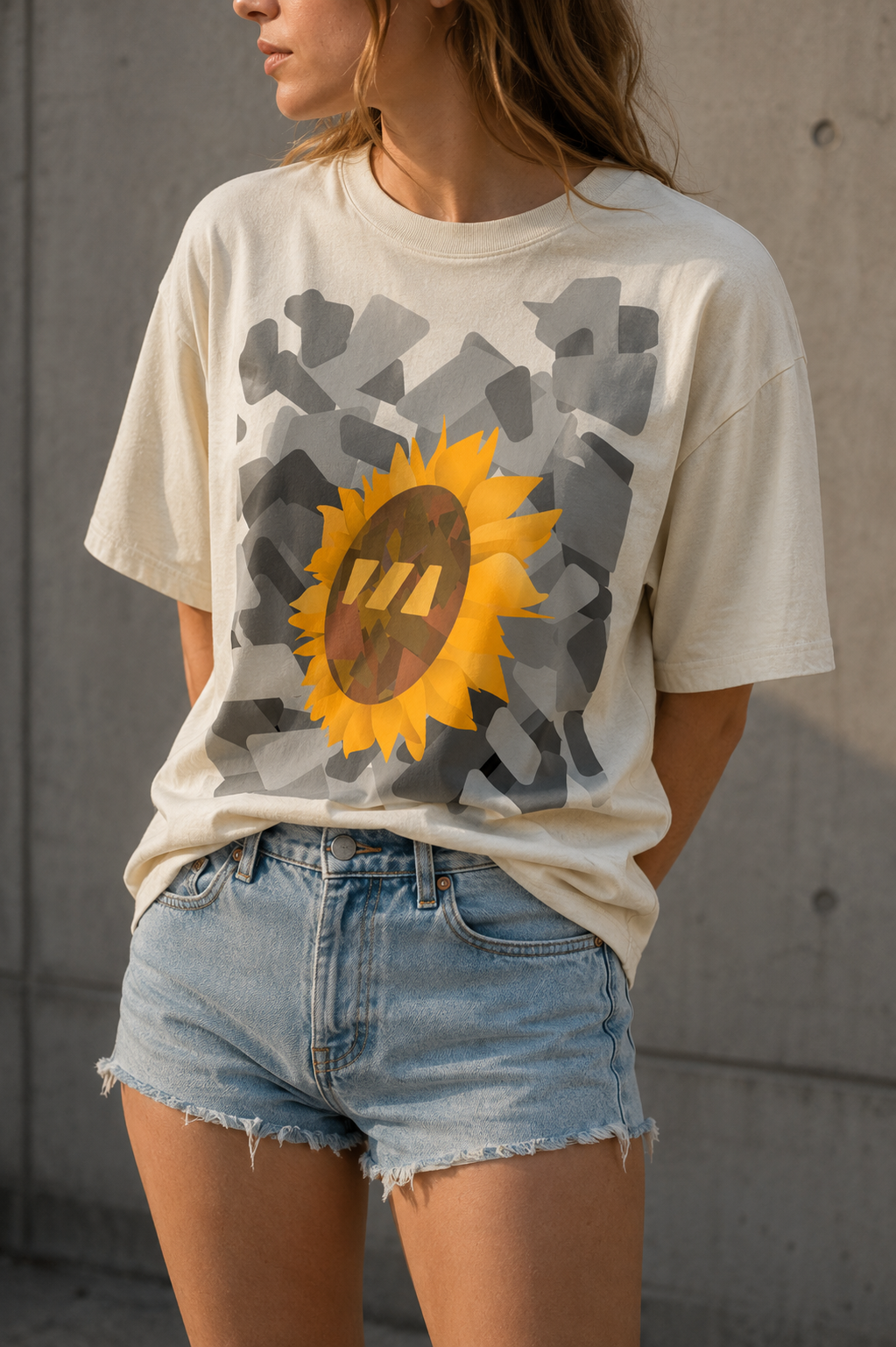 White girl standing with her hands behind her back, wearing an oversized off white tshirt with the City Sunflower Brekky Design on the front. The design features a sunflower head amidst grey monotone brekky logos arranged artistically.