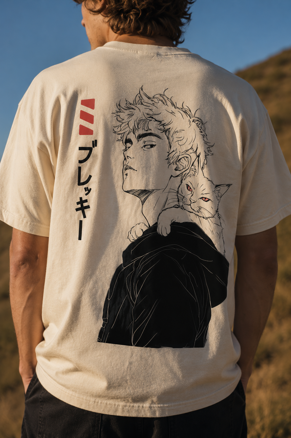 A white man stands by a hill, wearing a faded bone oversized t-shirt, with the "Orion and Rigel" character printed on the back. The accent color is red, and the text is black.