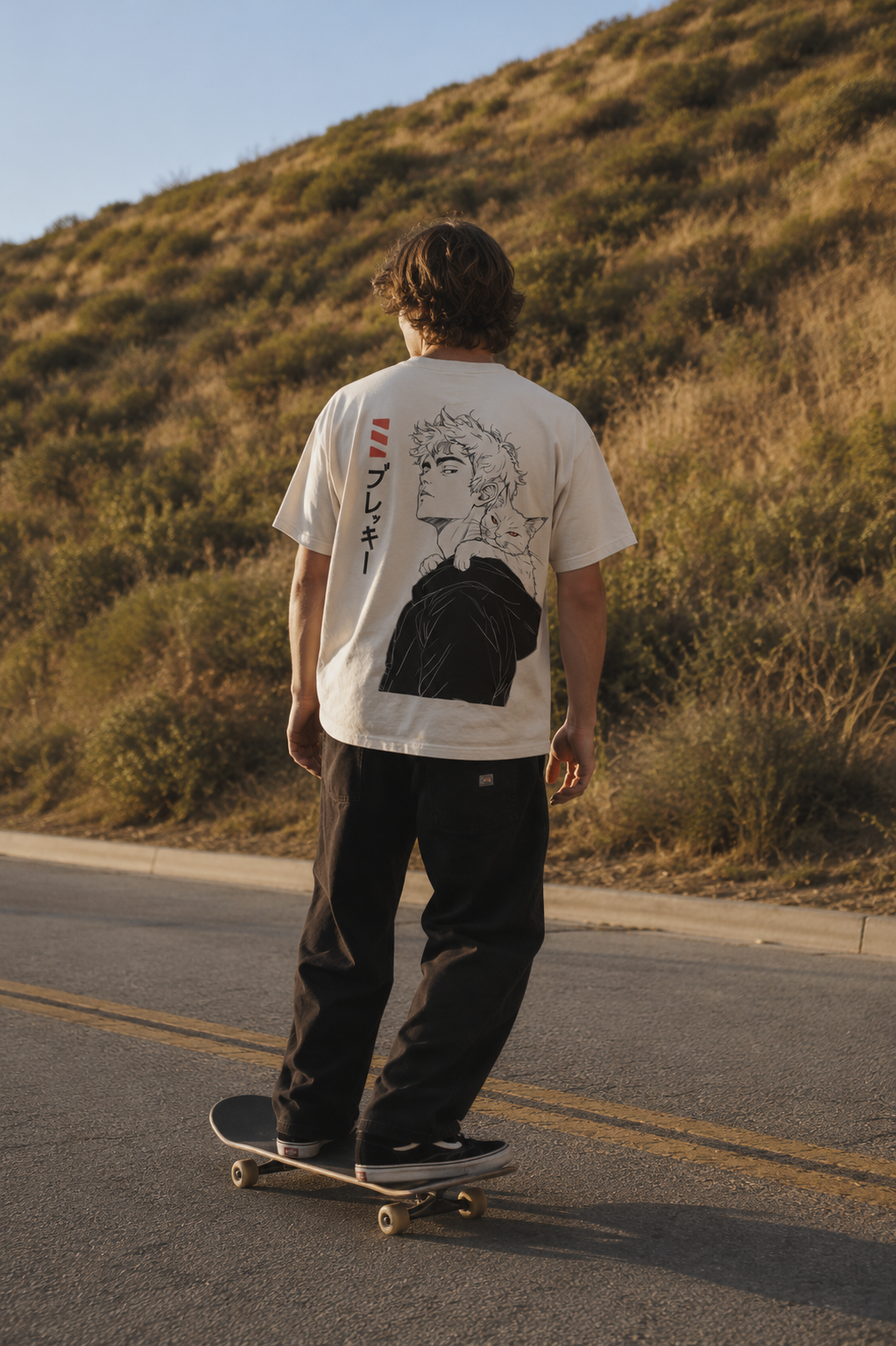 Man on a skateboard, traveling downhill casually. He is wearing an oversized white tshirt with a brekky design on the back. The design is Orion and Rigel, a man and hit cat, with "Brekky" spelled in katakana on the left side.
